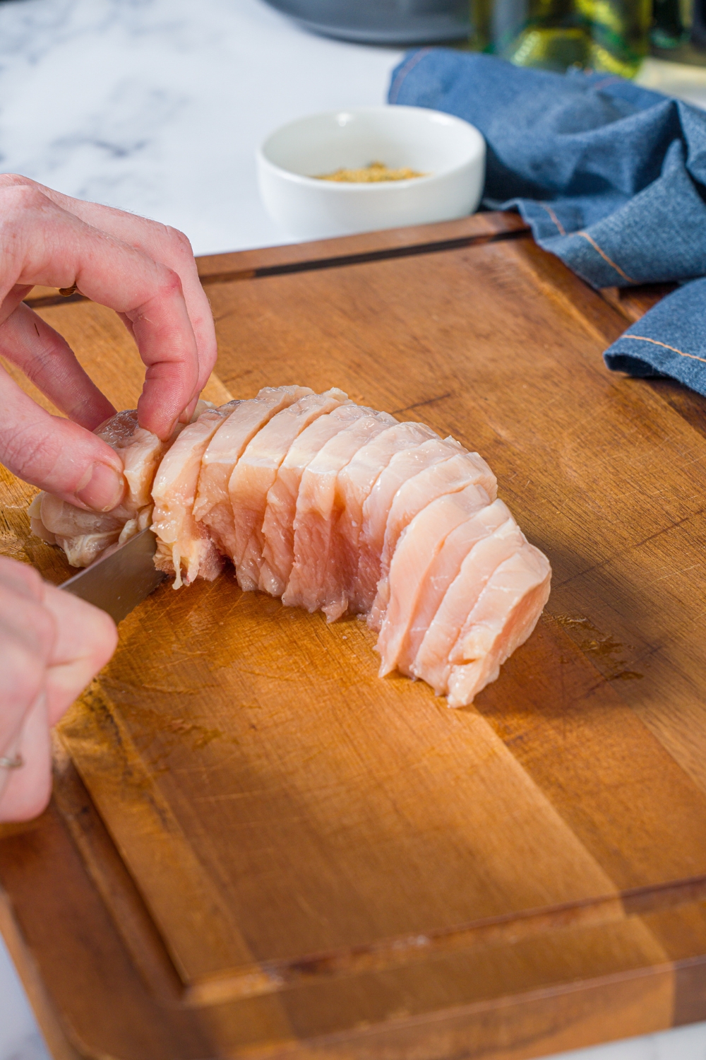 A cutting board with a defrosted chicken breast being sliced with a knife.