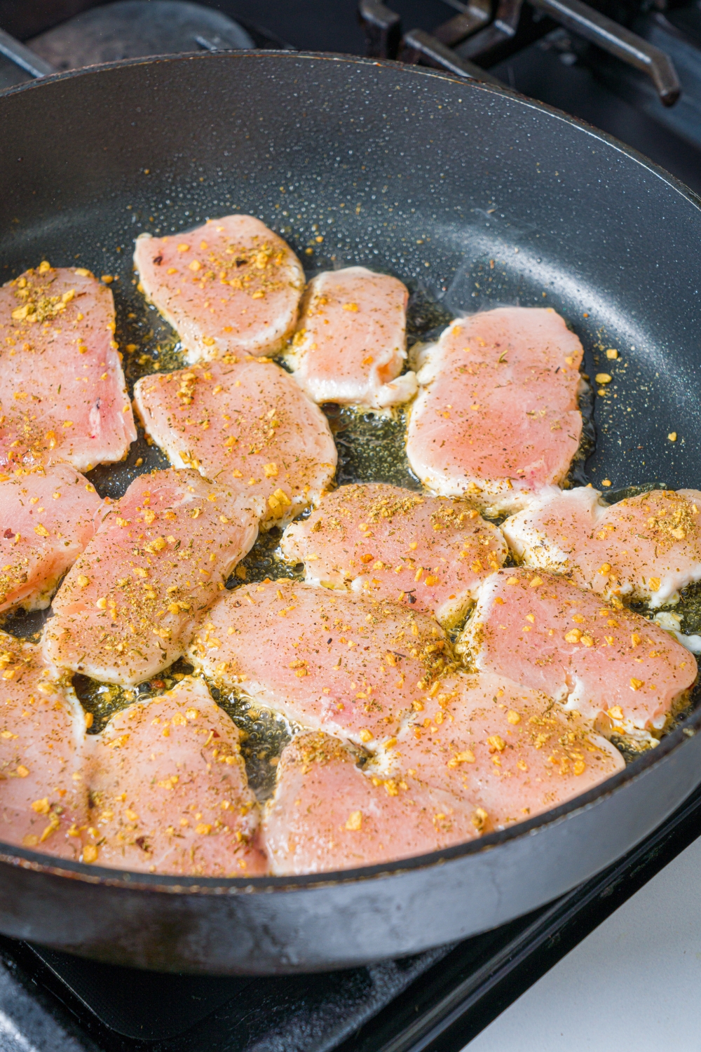 A skillet with sliced seasoned chicken breasts searing in oil.