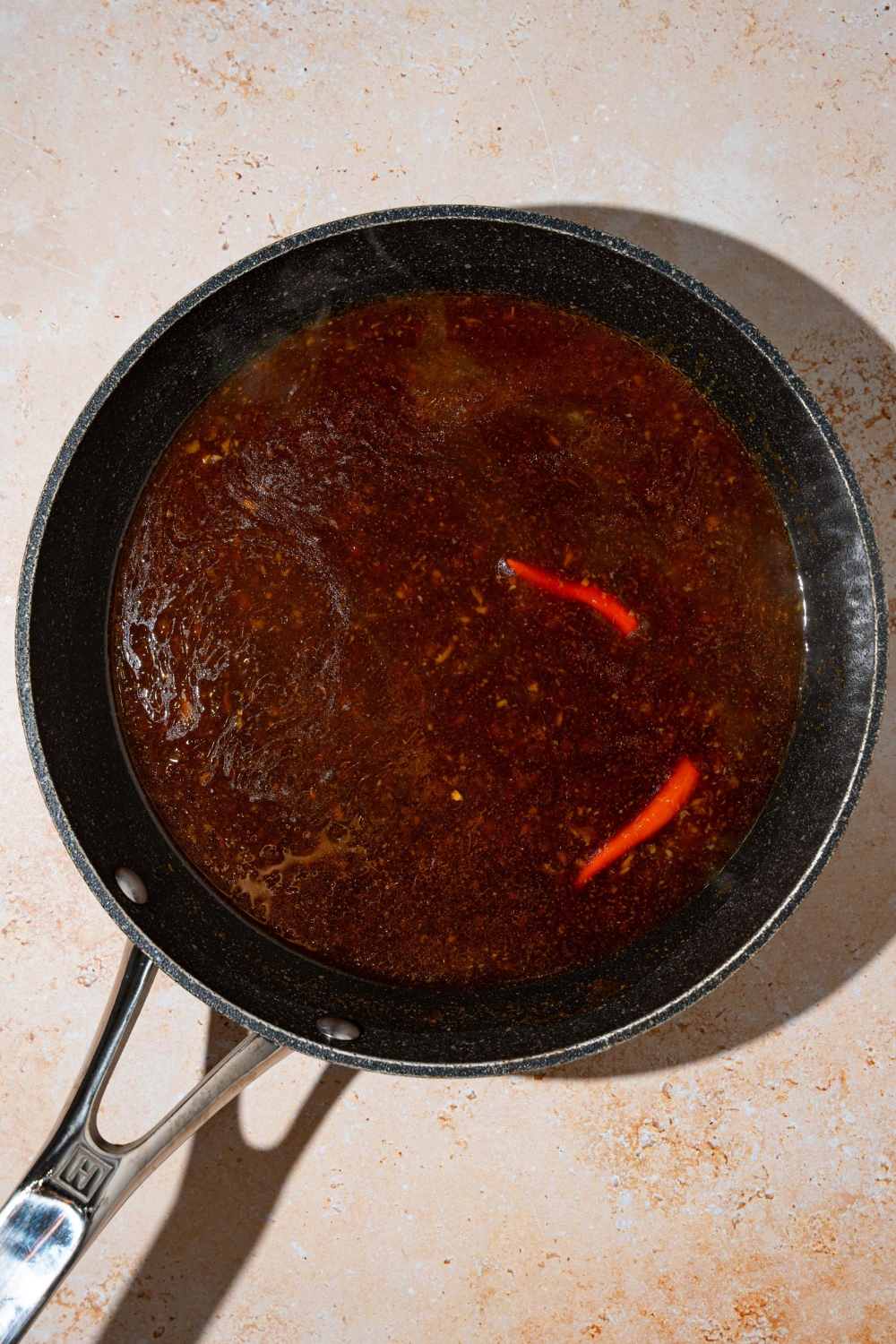 A skillet with cooked general tso sauce with red chiles. The skillet is on a tan counter.