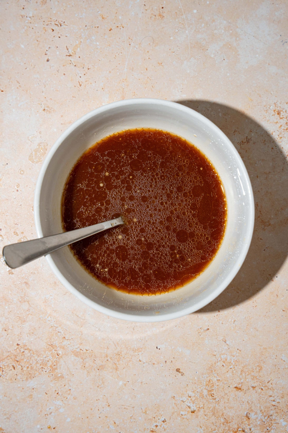A bowl with a general tso sauce mixture including soy sauce, hoisin, rice wine vinegar, and more. There is a spoon in the bowl.