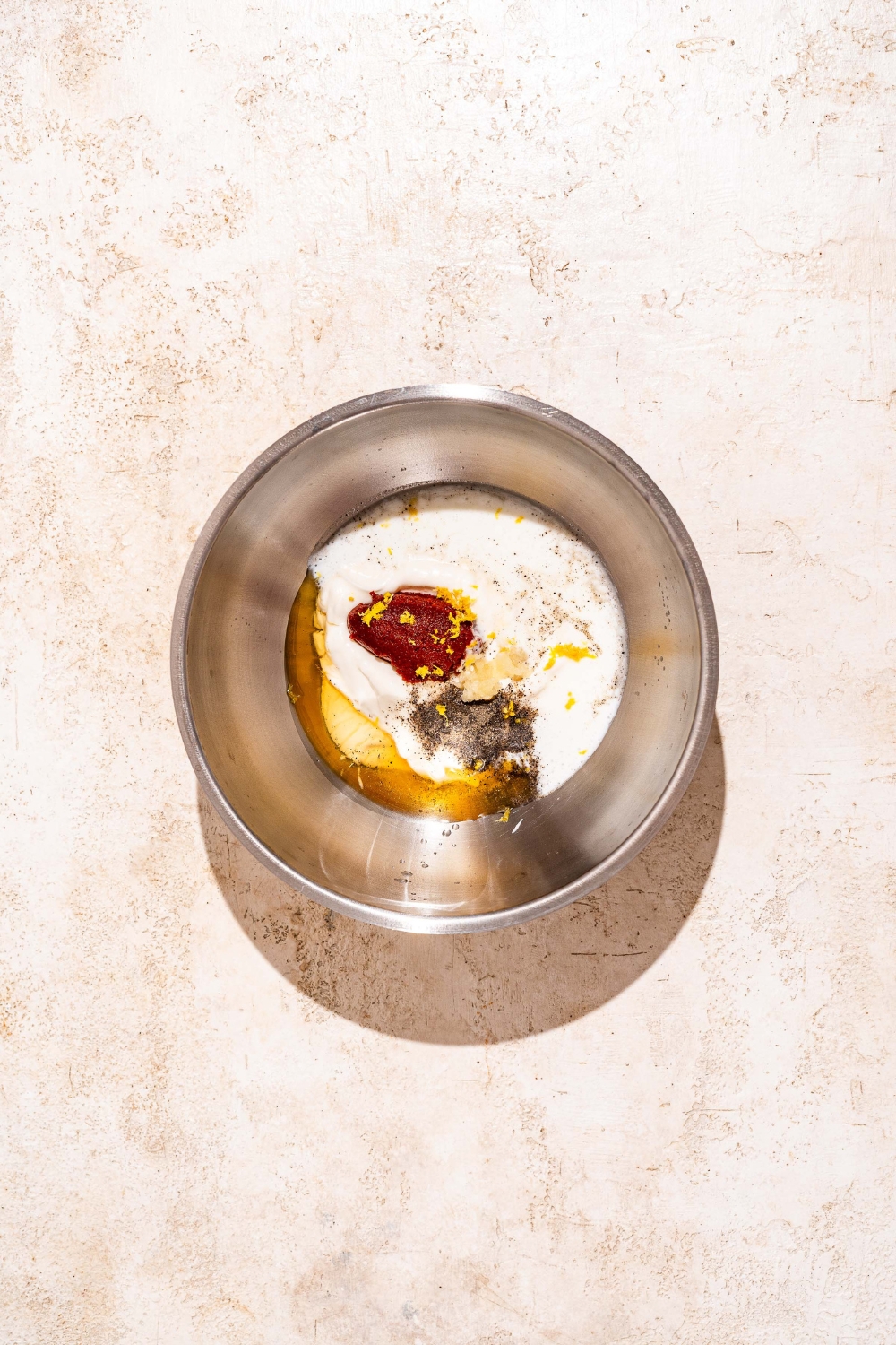 A large bowl with ingredients to make gochujang mayo including kewpie mayo, buttermilk, honey, gochujang, and garlic. The bowl is on a tan counter.