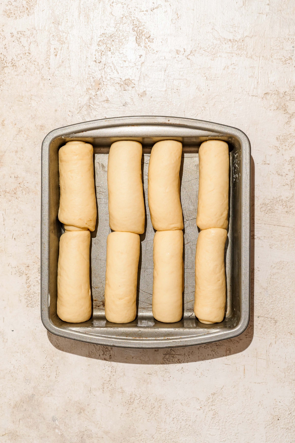 A large loaf pan with several pieces of rolled Raising Cane's bread dough. The pan is on a tan counter.