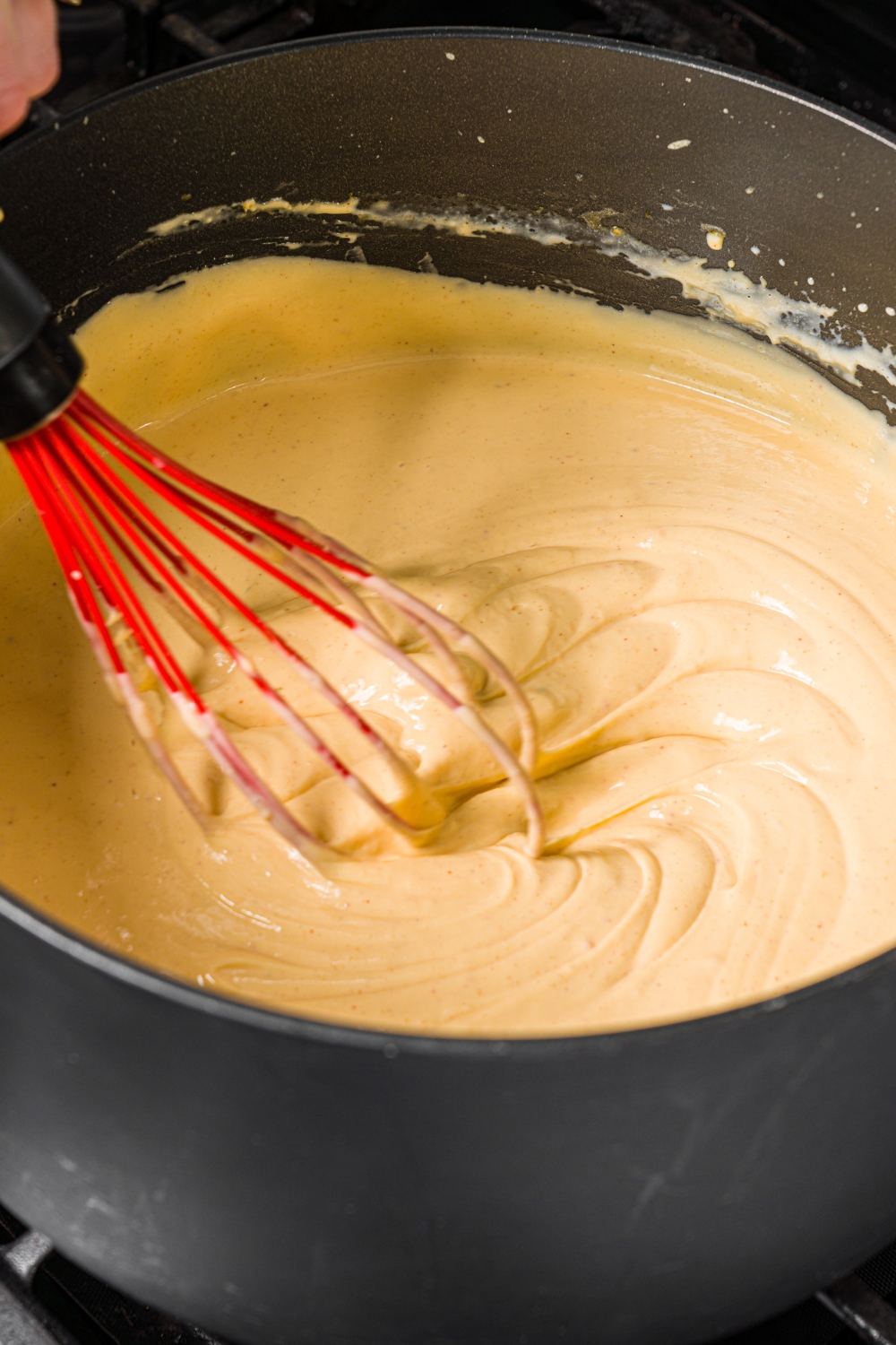 A large pot with a whisk mixing a creamy macaroni and cheese sauce.