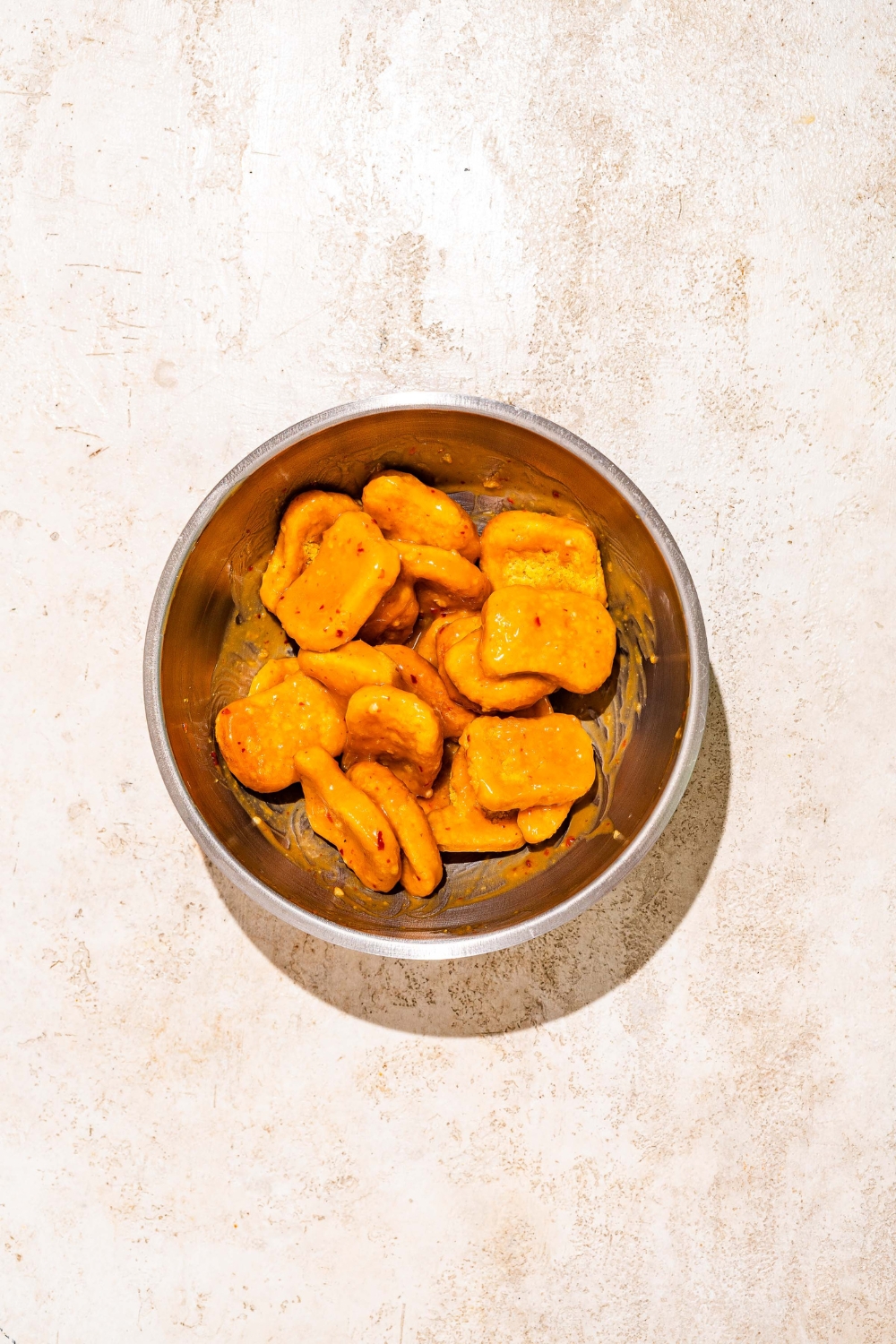 A bowl of chicken tossed in orange sauce. The bowl is on a tan counter.