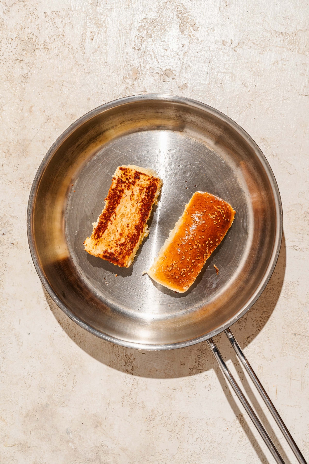 A skillet with a baked Raising Cane's bread loaf sliced in half and toasting on the skillet. The skillet is on a tan counter.