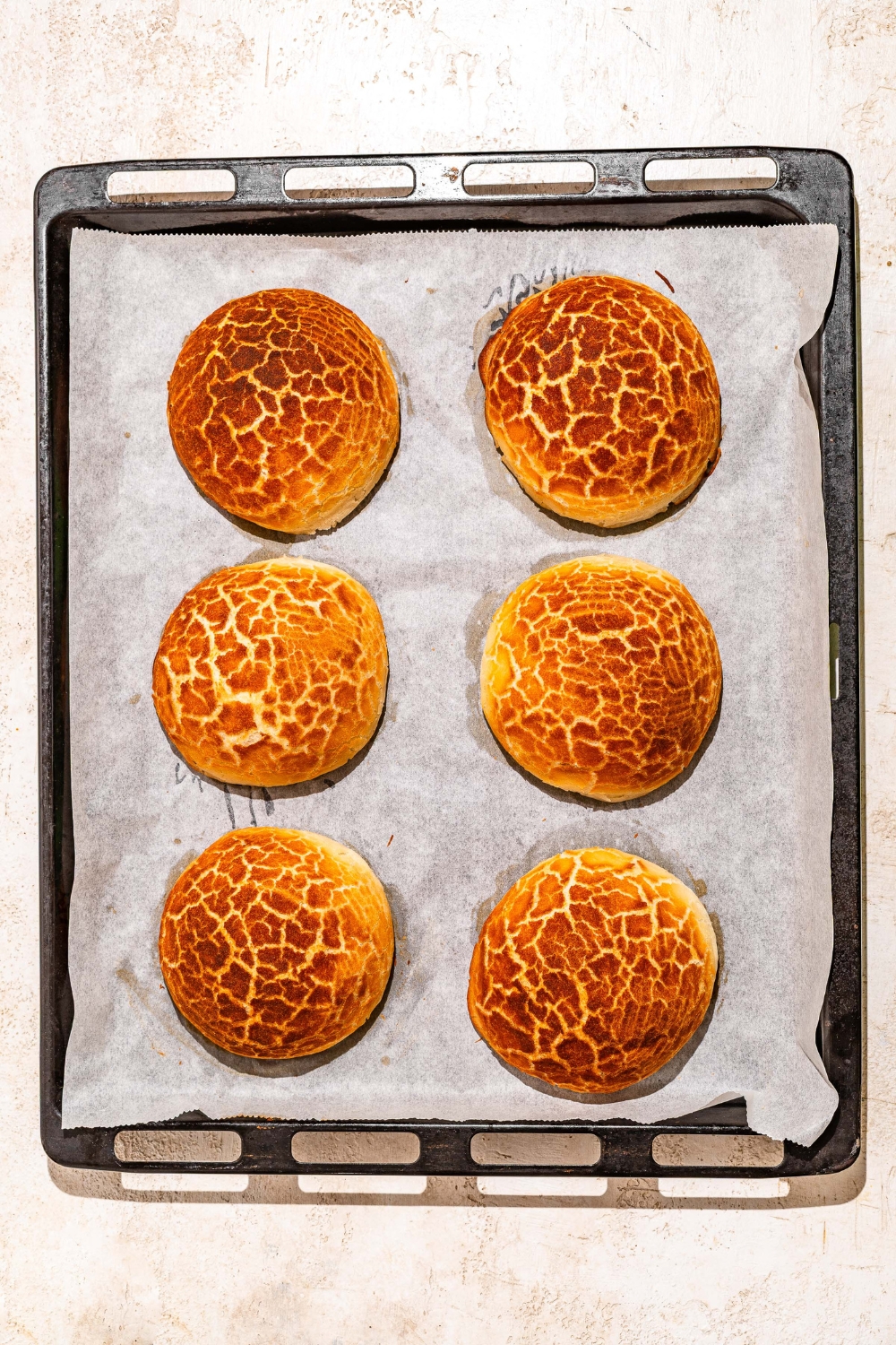 A lined baking sheet with baked Dutch Crunch bread loaves. The sheet is on a tan counter.