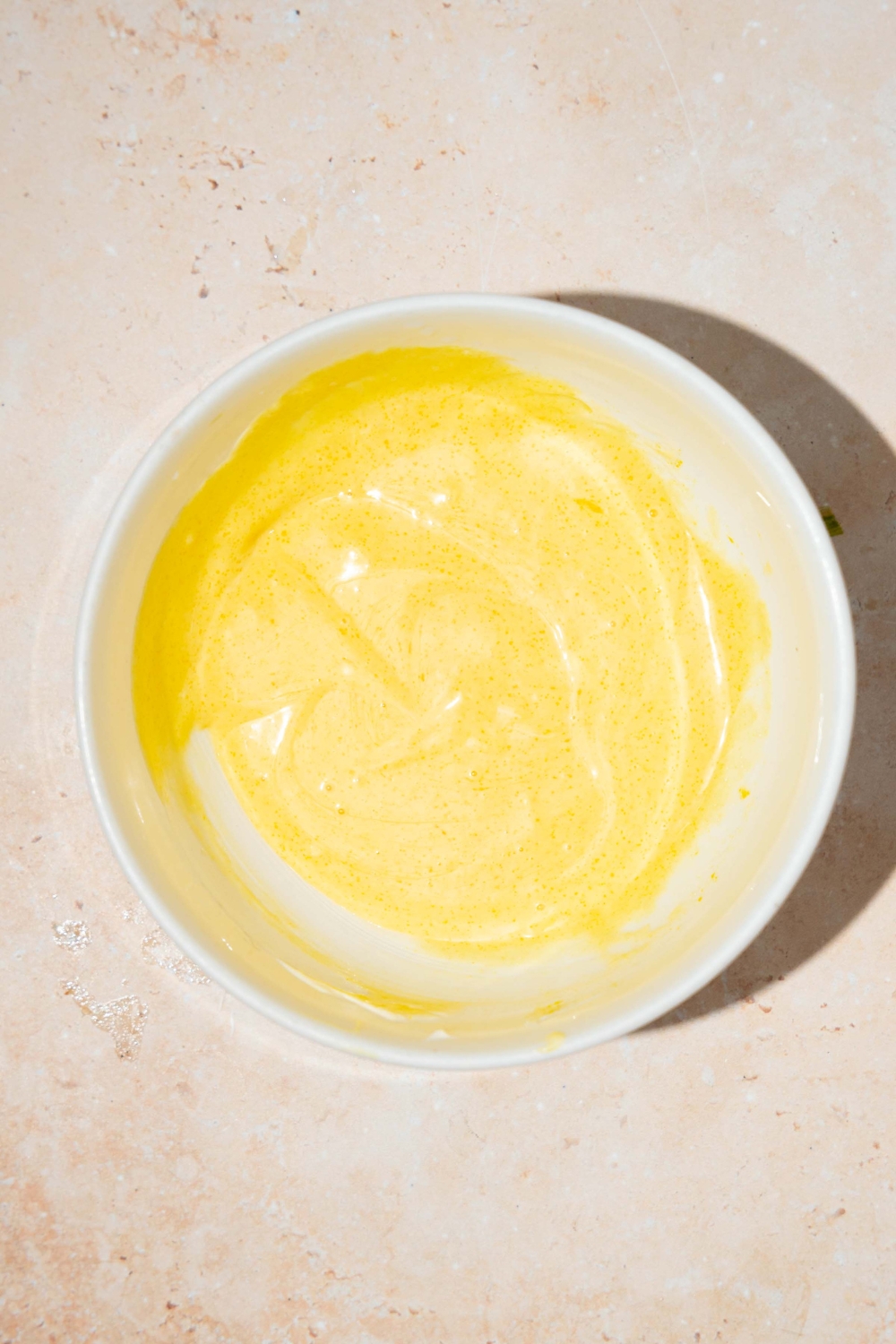 A bowl with mixed honey mustard sauce including mayo, yellow mustard, dijon mustard, honey, and lemon. The bowl is on a tan counter.