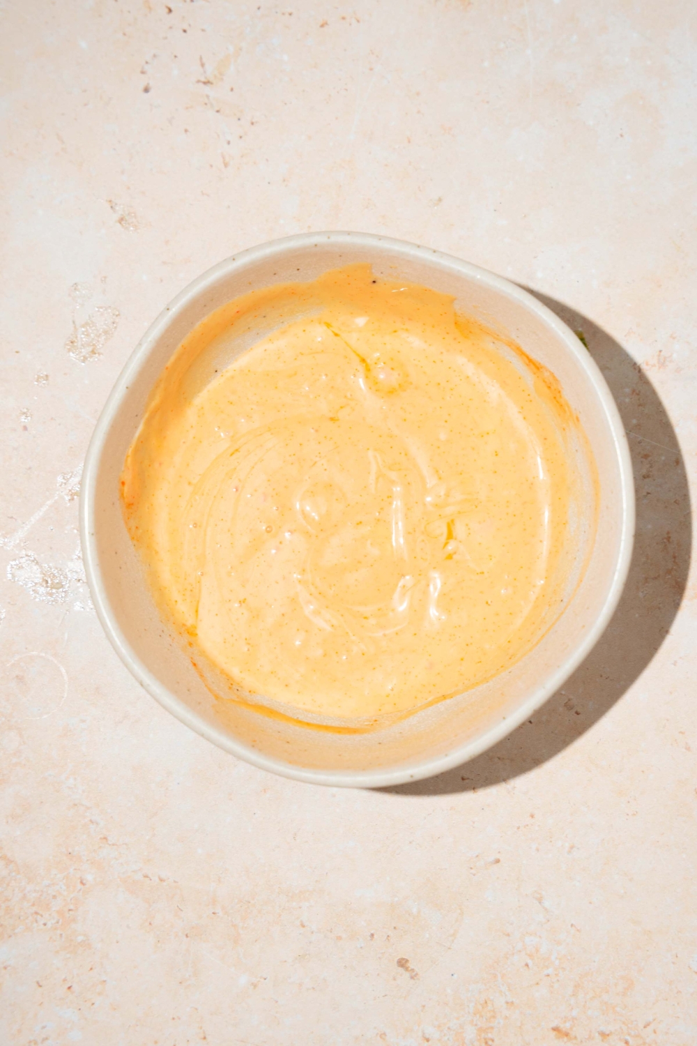 A bowl of mixed honey sriracha sauce. The bowl is on a tan counter.