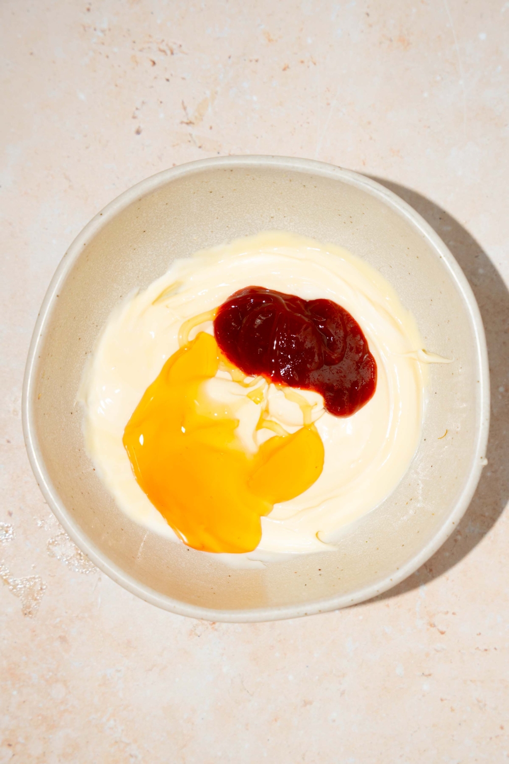 A bowl with ingredients to make honey sriracha sauce including mayo, honey, and sriracha.