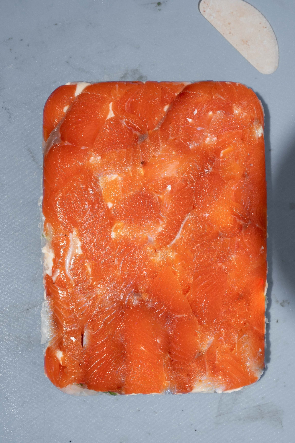 A blue counter with a flipped baking dish of lazy sushi topped with smoked salmon.