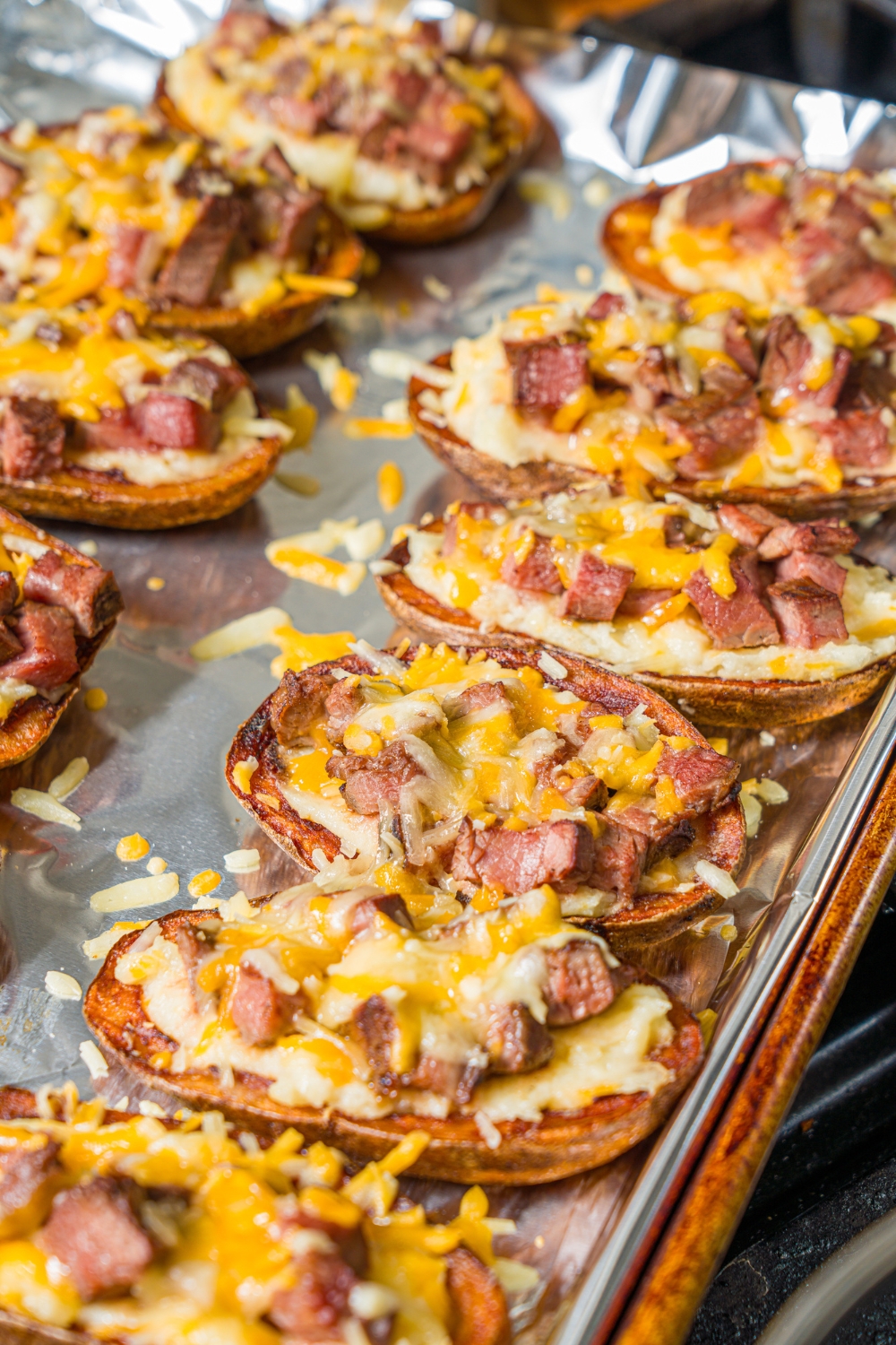 A baking sheet lined with foil with baked steak loaded potato skins.