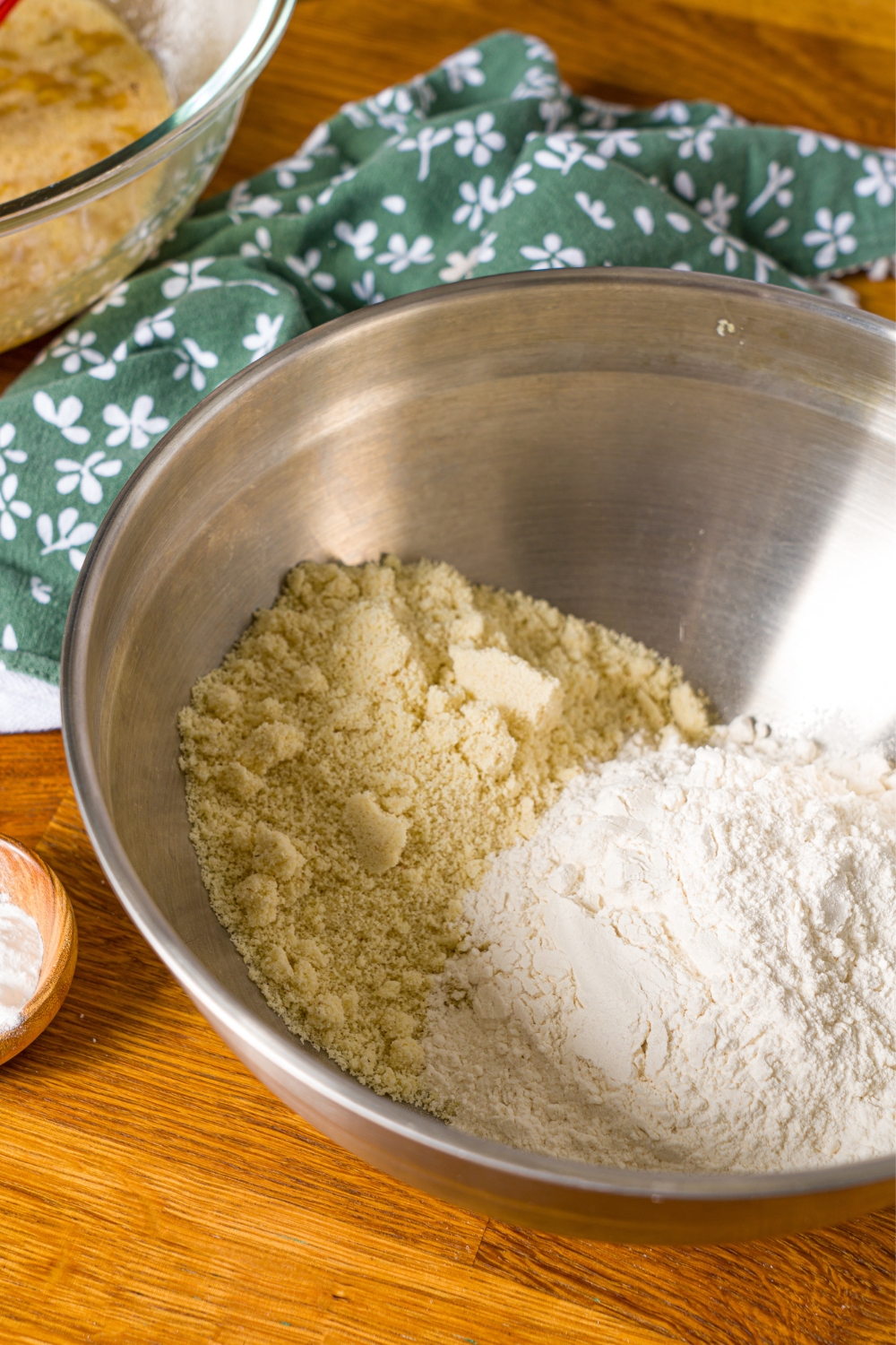 A large bowl with dry ingredients to make banana bread with olive oil. The bowl is on a wooden counter with a green floral napkin.
