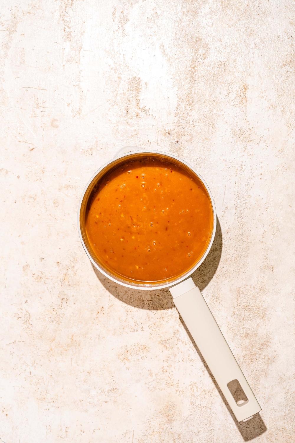 A saucepan with cooked orange sauce. The saucepan is on a tan counter.