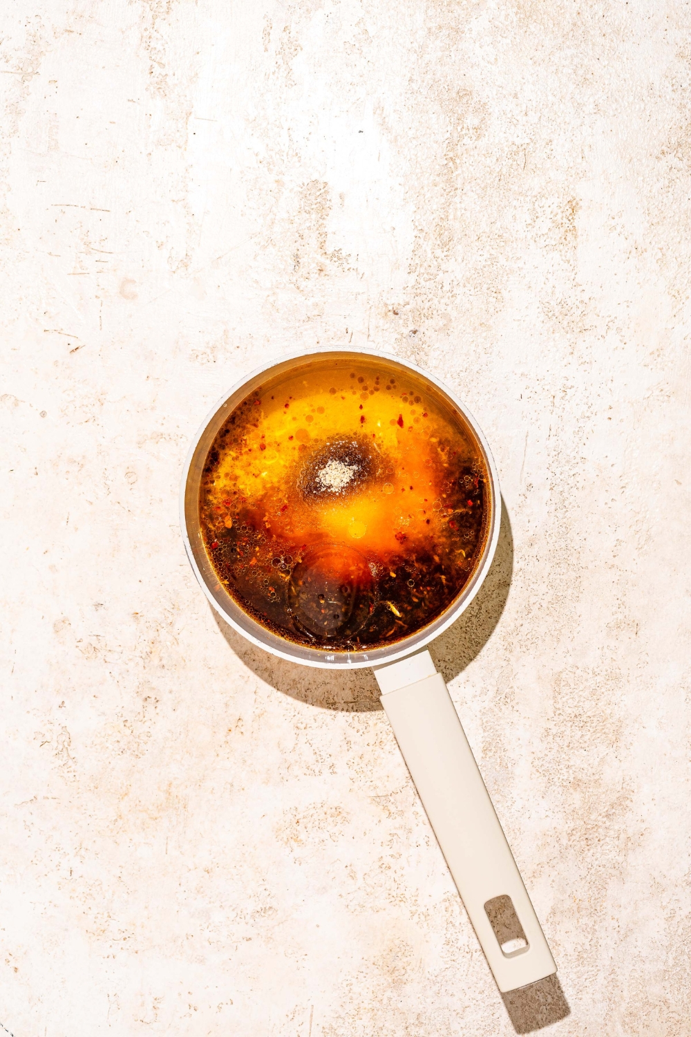 A saucepan with juices being added to a saucepan to make orange sauce. The saucepan is on a tan counter.