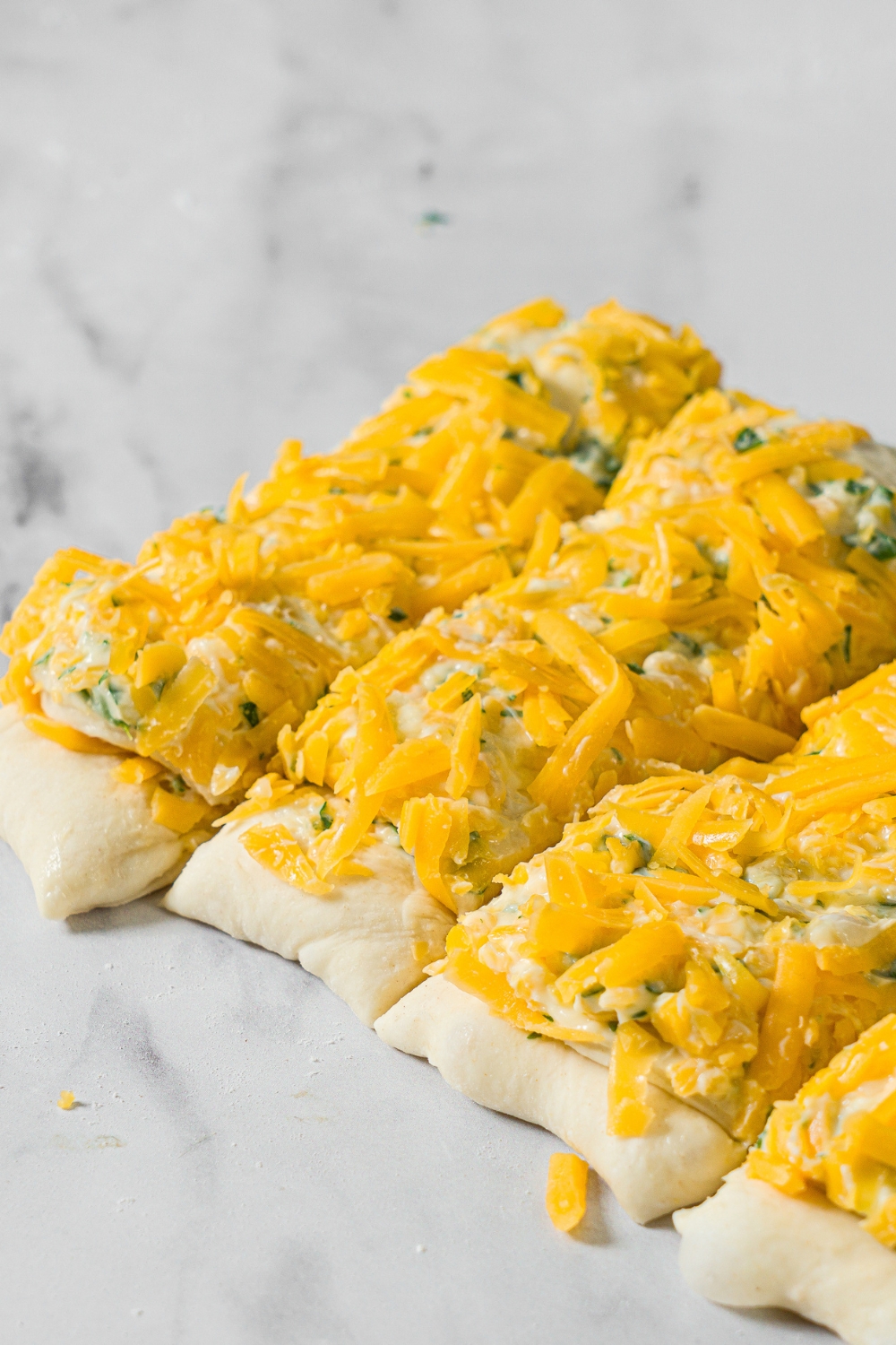 Pull apart garlic bread dough topped with garlic butter and shredded cheese. The dough is sliced into horizontal pieces.