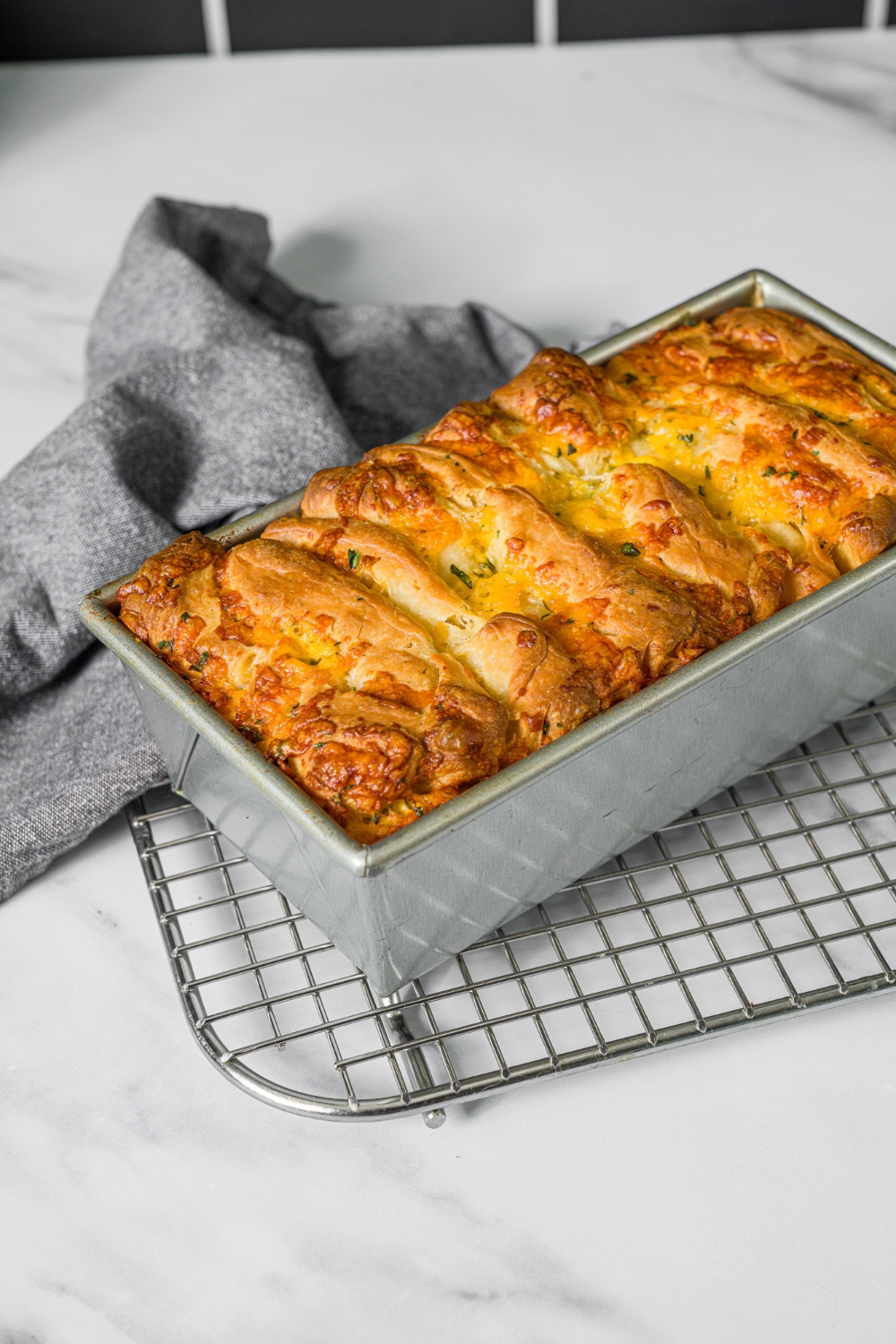 A loaf pan with baked pull apart cheesy garlic bread. The pan is on a wire rack on a marble counter.