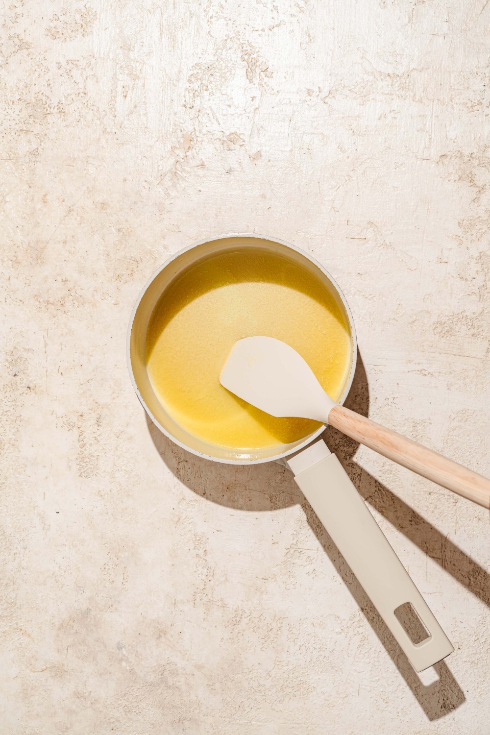 A saucepan with a spatula mixing a honey butter glaze. The saucepan is on a tan counter.