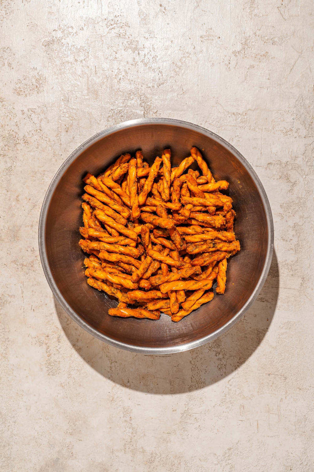 A large bowl with pretzel braids tossed in boil and seasonings. The bowl is on a tan counter.