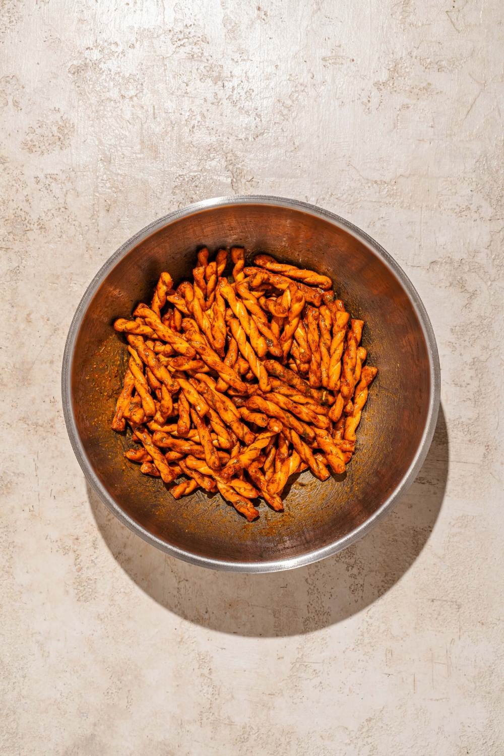 A large bowl with pretzel braids tossed in boil and seasonings. The bowl is on a tan counter.