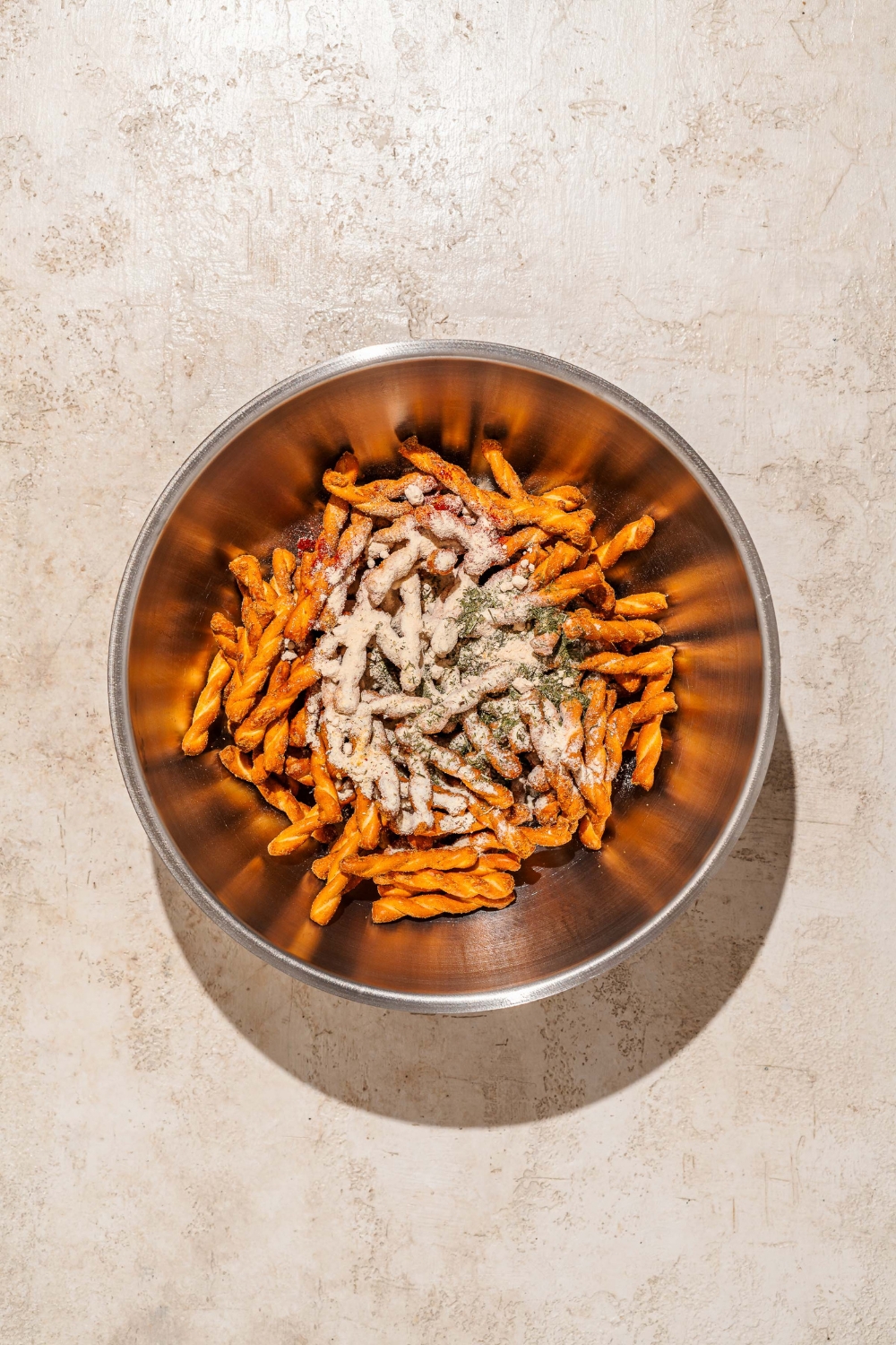 A large bowl of pretzel braids topped with seasonings. The bowl is on a tan counter.