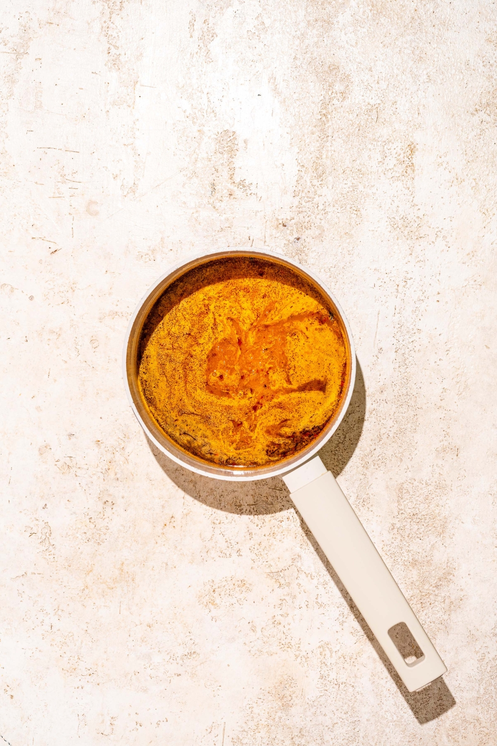 A saucepan with a slurry added to an orange sauce base. The saucepan is on a tan counter.