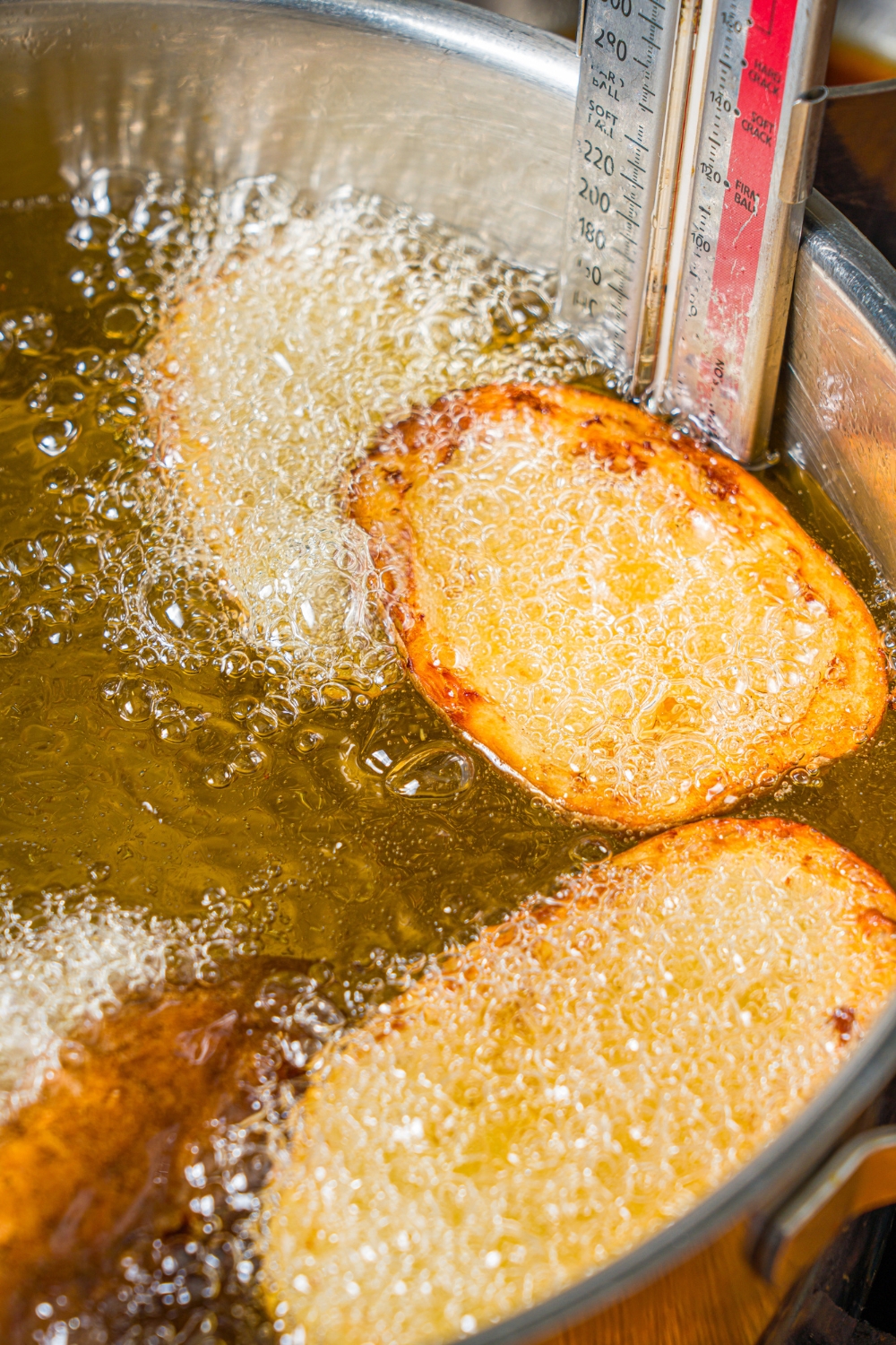 A large pot with frying oil and several potato skins frying in the oil.
