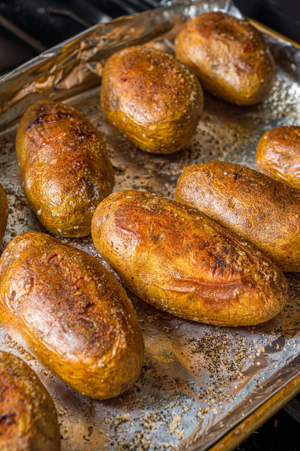 A baking sheet lined with foil with several seasoned and baked potatoes.