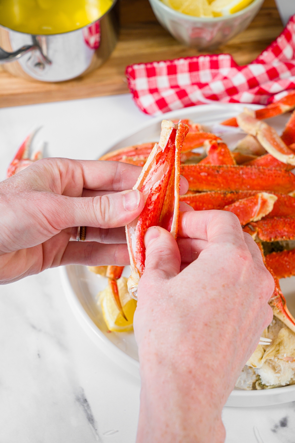 A white plate with steamed snow crab legs. One of the legs is being opened.