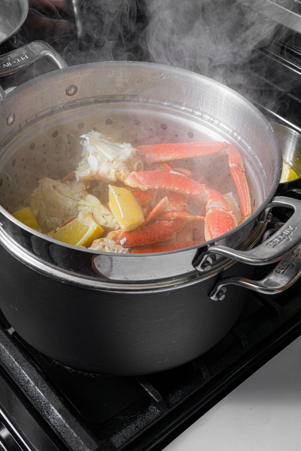 A large pot with a steamer basket of snow crab legs steaming with lemon.