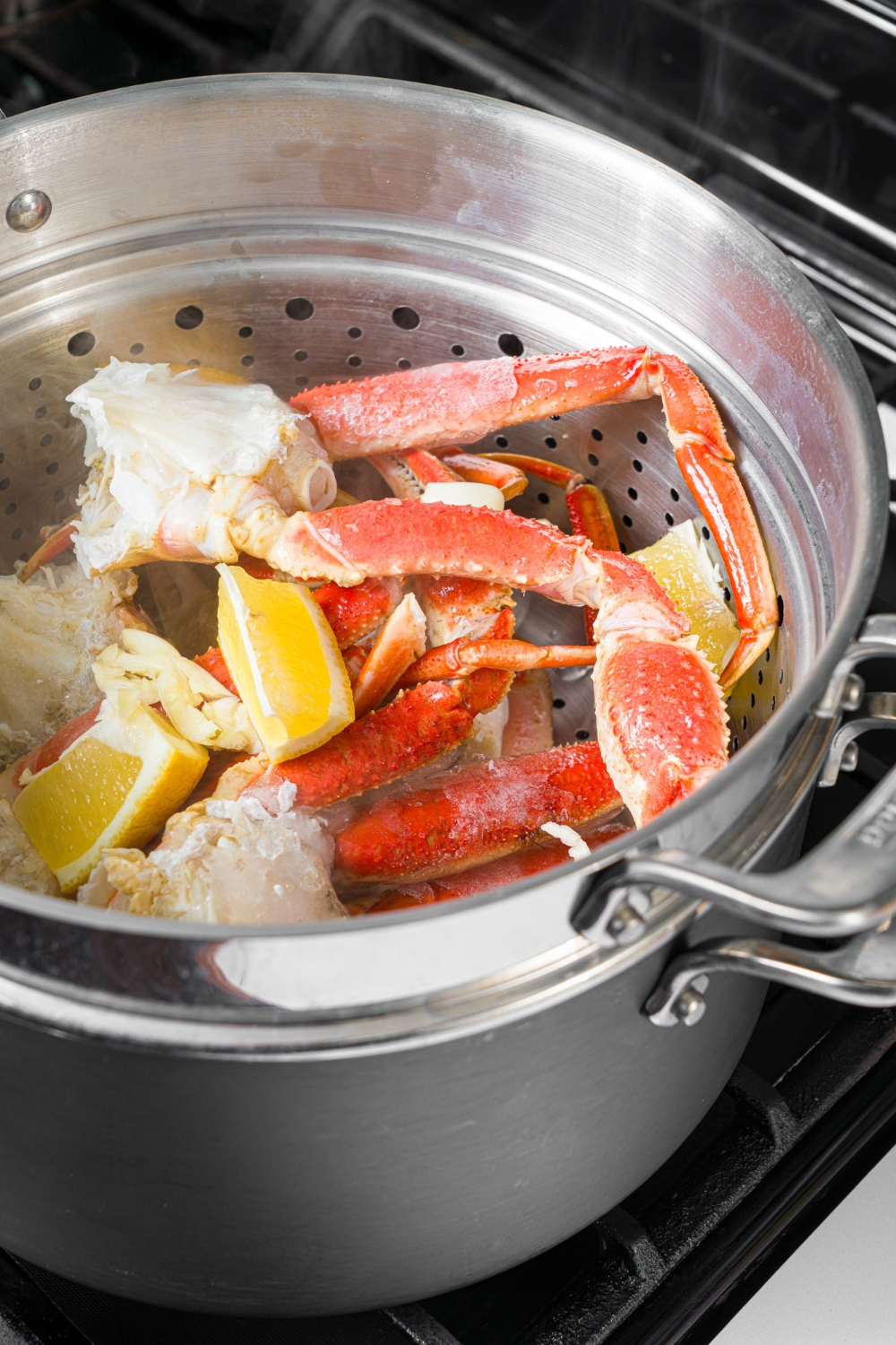 A large pot with a steamer basket with snow crab legs and lemon.