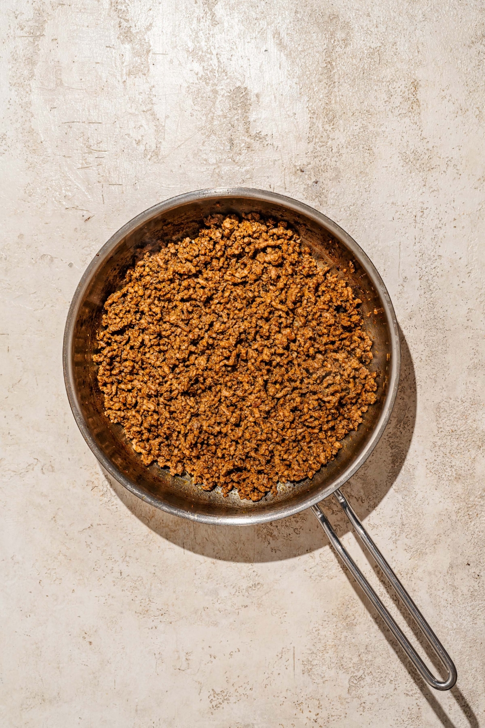 A skillet with seasoned ground beef. The skillet is on a tan counter.