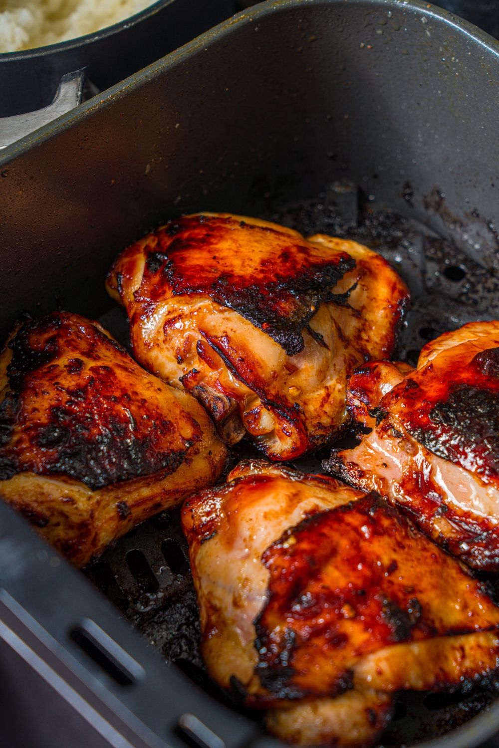 Four pieces of chicken teriyaki cooking in an air fryer basket.