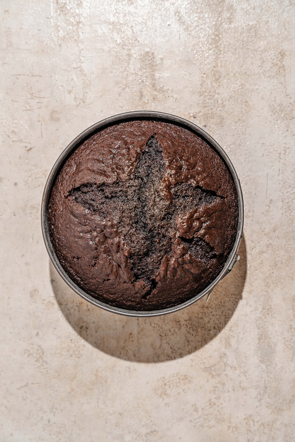 A cake tin with baked chocolate cake. The tin is on a tan counter.