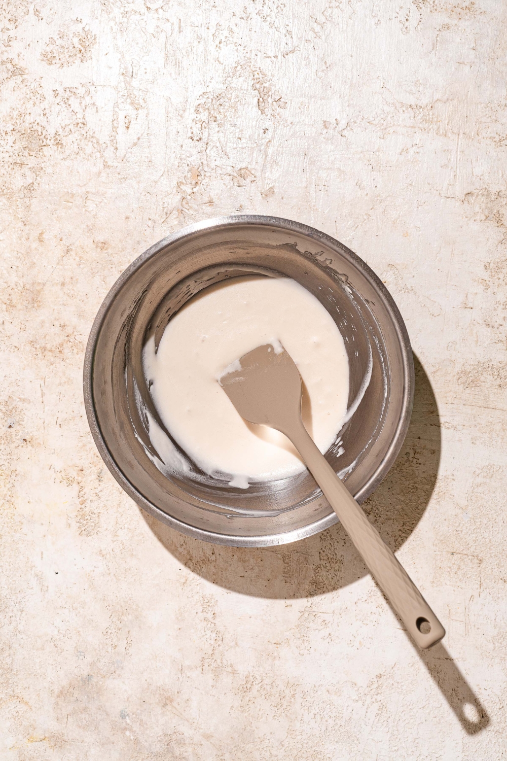 A large bowl with a spatula mixing ingredients to make Dutch Crunch topping. The bowl is on a tan counter.