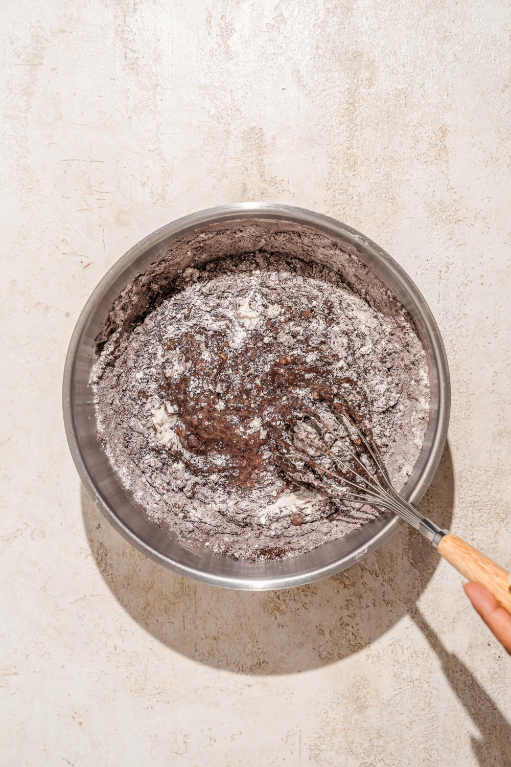 A large mixing bowl with a whisk mixing dry ingredients with a wet mixture to make chocolate cake.