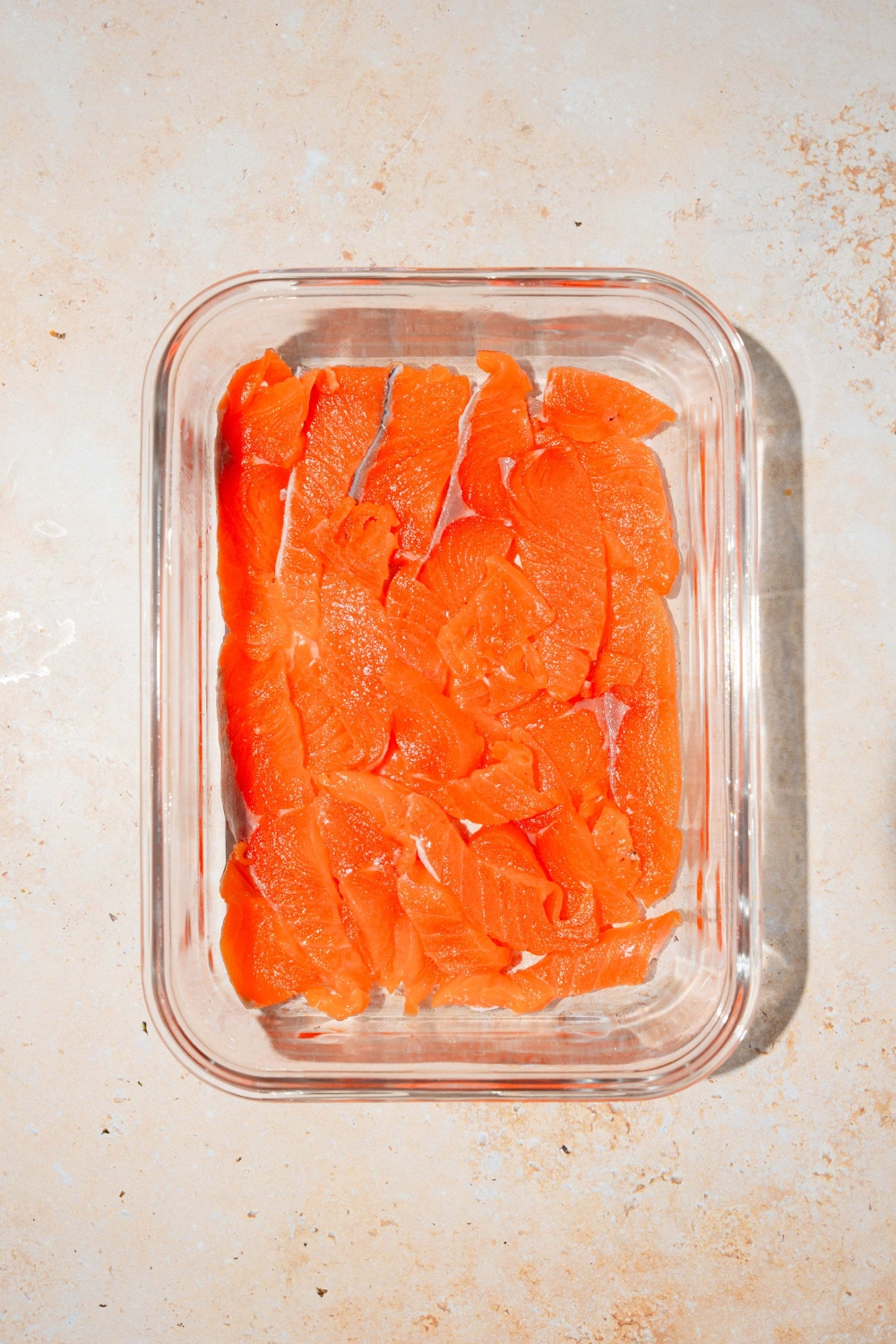 A baking dish covered with smoked salmon. The dish is on a tan counter.