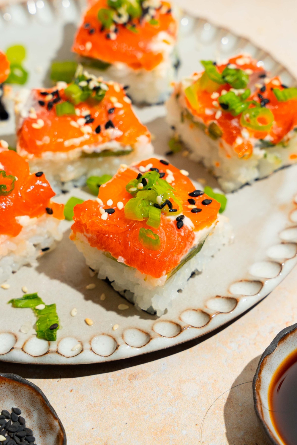 A plate of lazy sushi with salmon topped with sliced green onion and sesame seeds. The plate is on a tan counter.