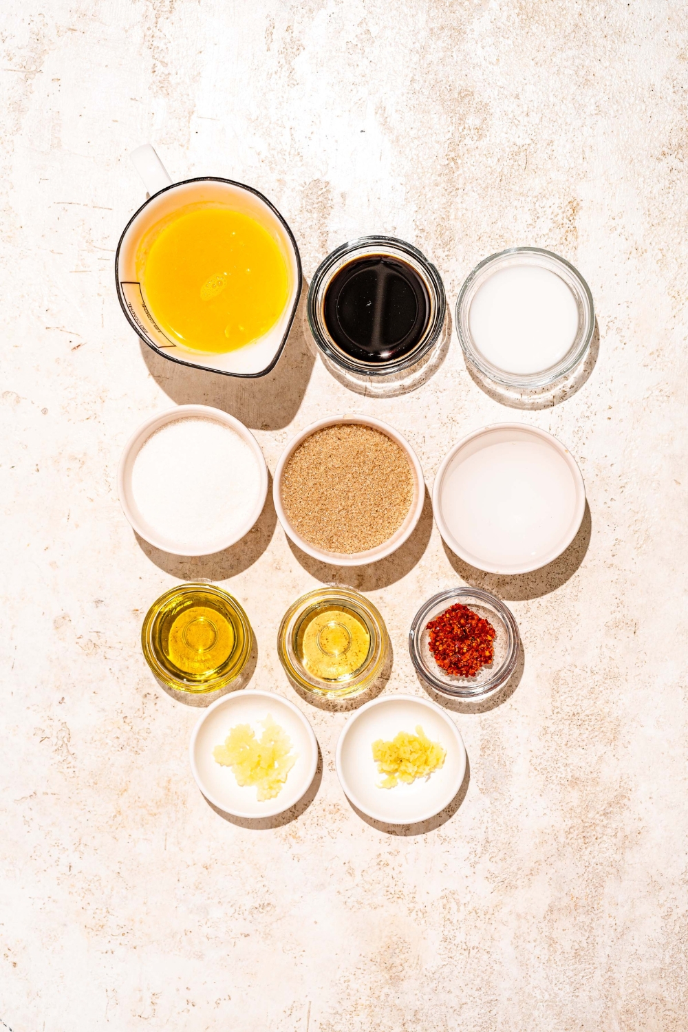 A tan counter with several bowls containing ingredients to make orange sauce including orange juice, soy sauce, vinegar, brown sugar, cornstarch, sesame oil, and more.