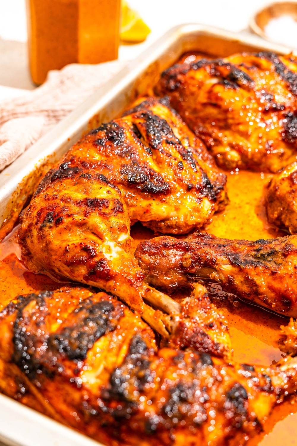 A sheet pan with roasted chicken cooked in peri peri sauce. The pan is on a tan counter with a jar of sauce.