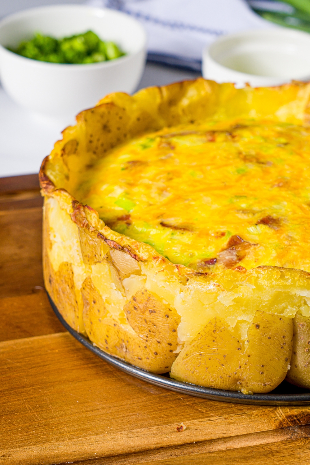 A wooden board with an open springform pan with baked potato crust quiche.