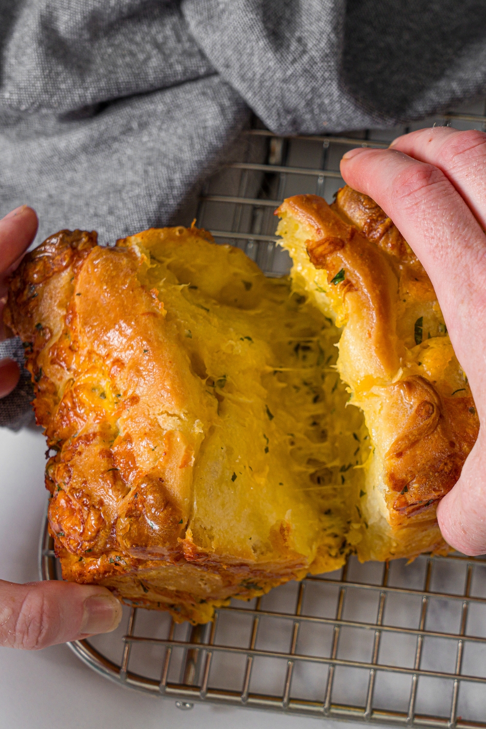 A wire rack with a loaf of pull apart garlic bread. A hand is pulling up a piece of bread.