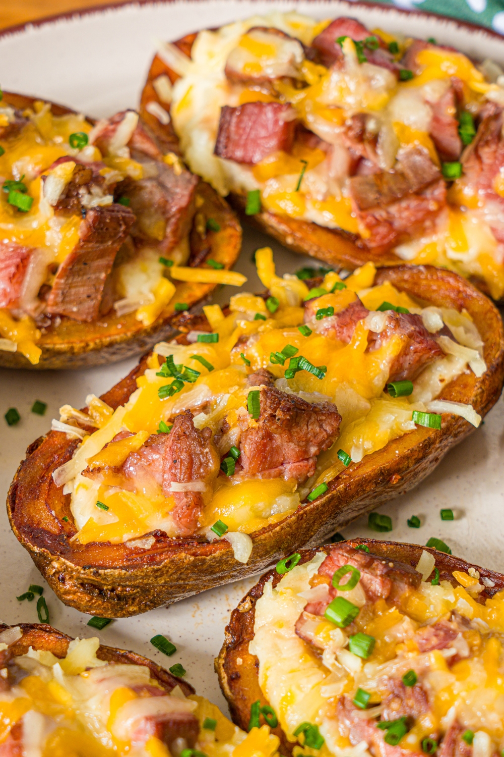 A white plate with several steak loaded potato skins with melted cheese on top and garnished with sliced chives.