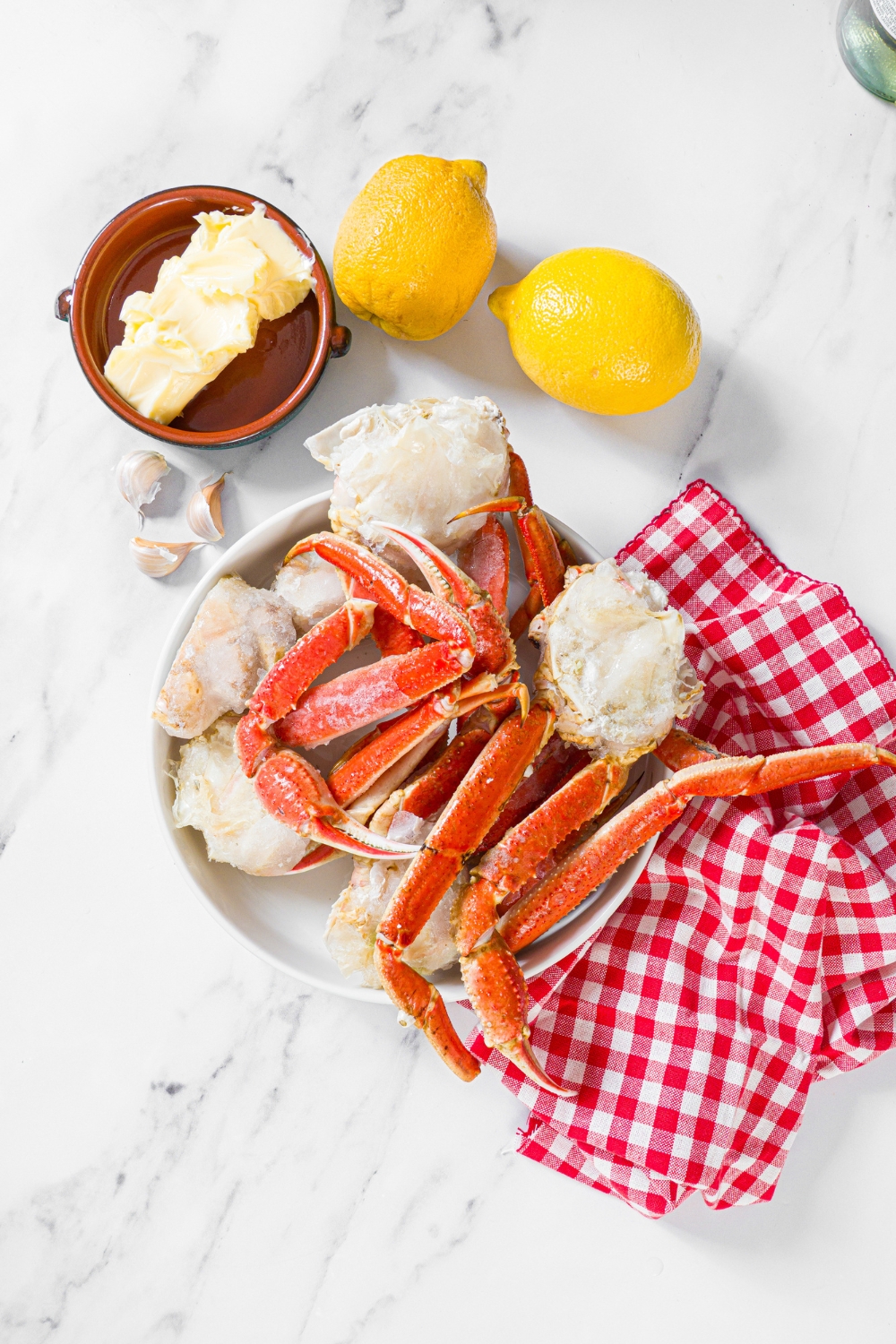 A marble counter with ingredients to make steamed snow crab legs including crab legs, lemon, garlic, and butter.