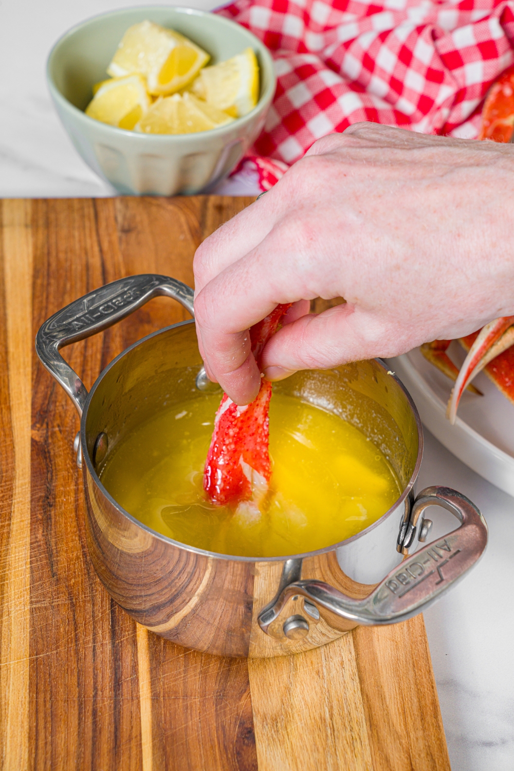 A small saucepan of garlic lemon sauce with a piece of crab meat being dipped in the sauce. The saucepan is on a wooden board.