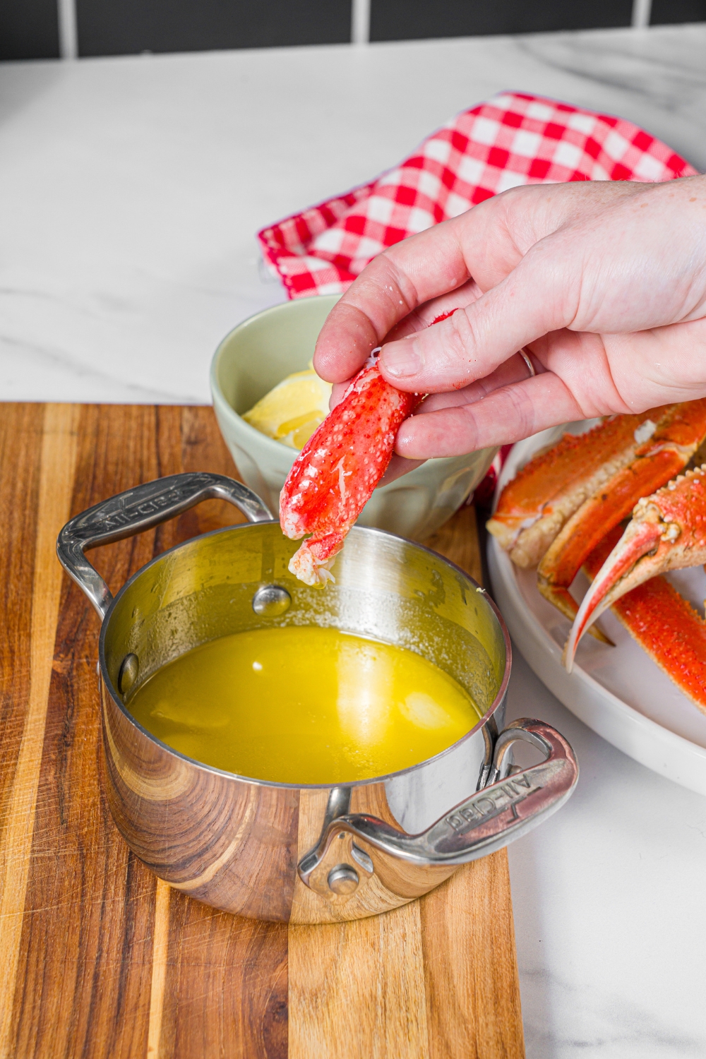 A small saucepan of garlic lemon sauce with a piece of crab meat being dipped in the sauce. The saucepan is on a wooden board.