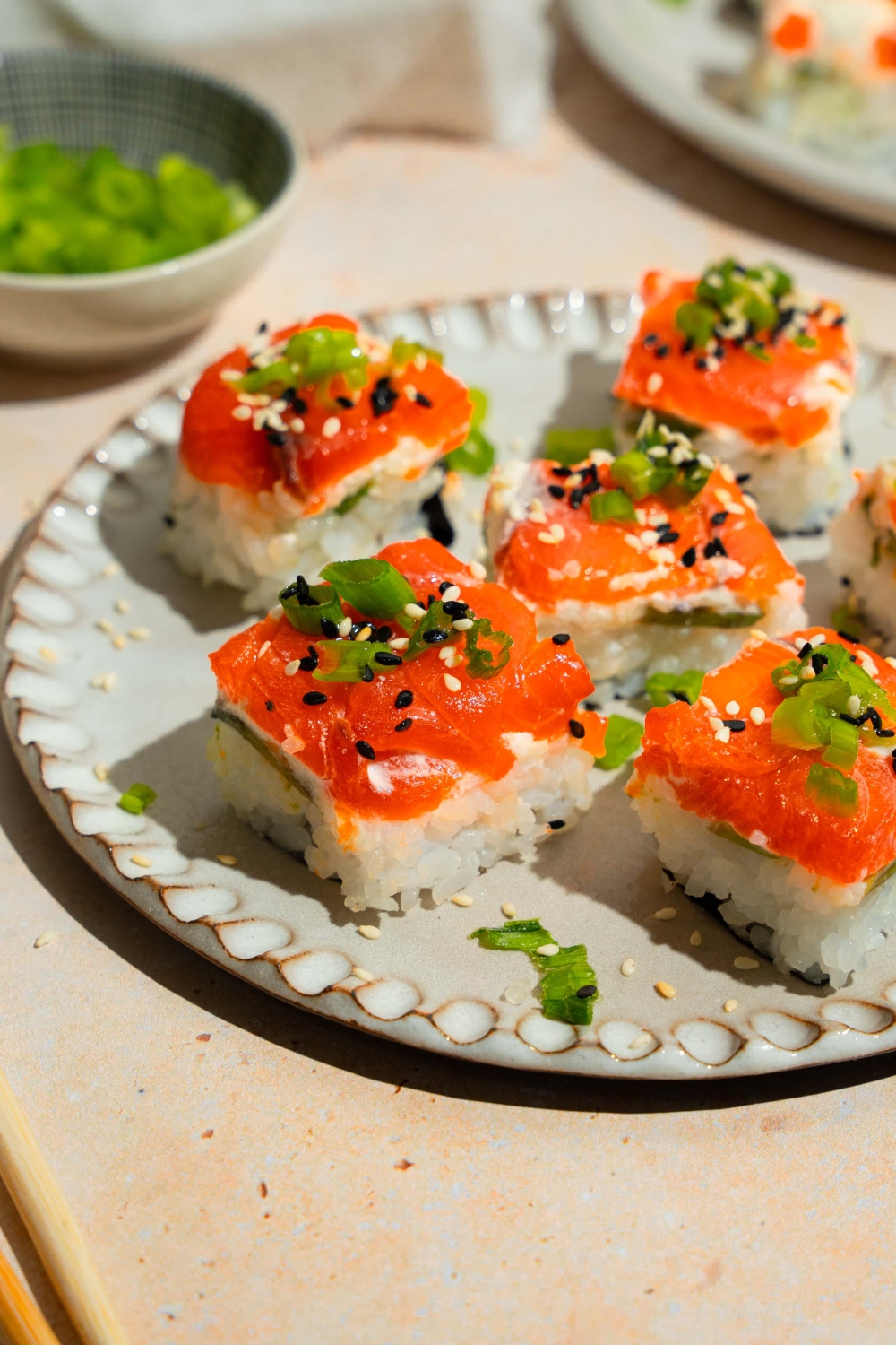 A plate of lazy sushi with salmon topped with sliced green onion and sesame seeds. The plate is on a tan counter.