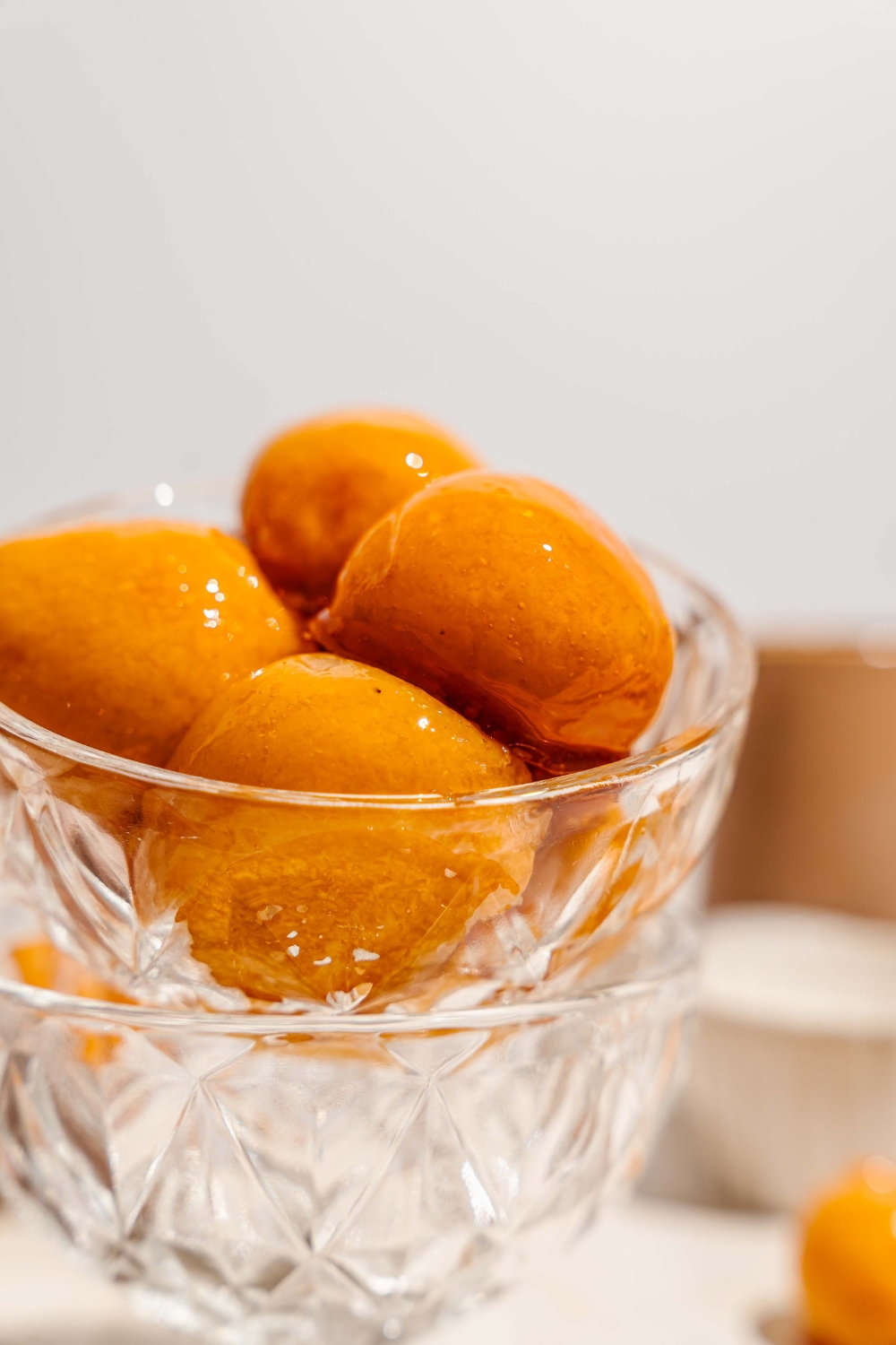 A glass bowl with several pieces of bala baiana balls stacked in another glass bowl. The bowl is on a tan counter.
