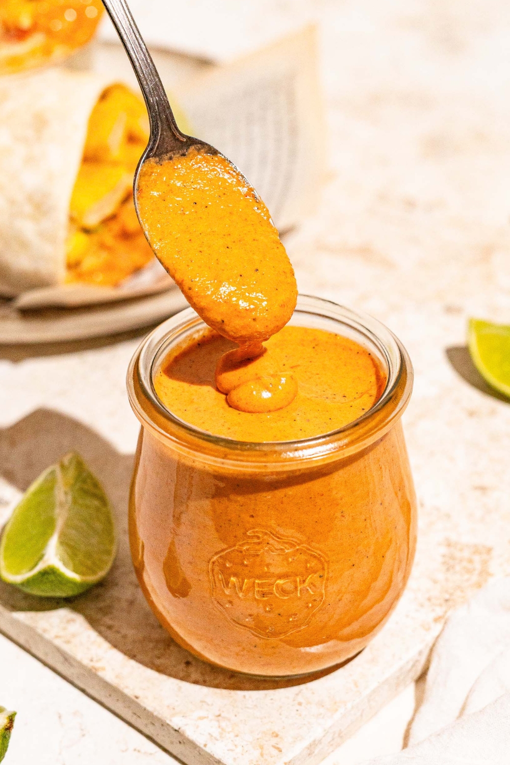 A spoon covered in burrito sauce drizzling it into a glass jar that is filled with the burrito sauce.