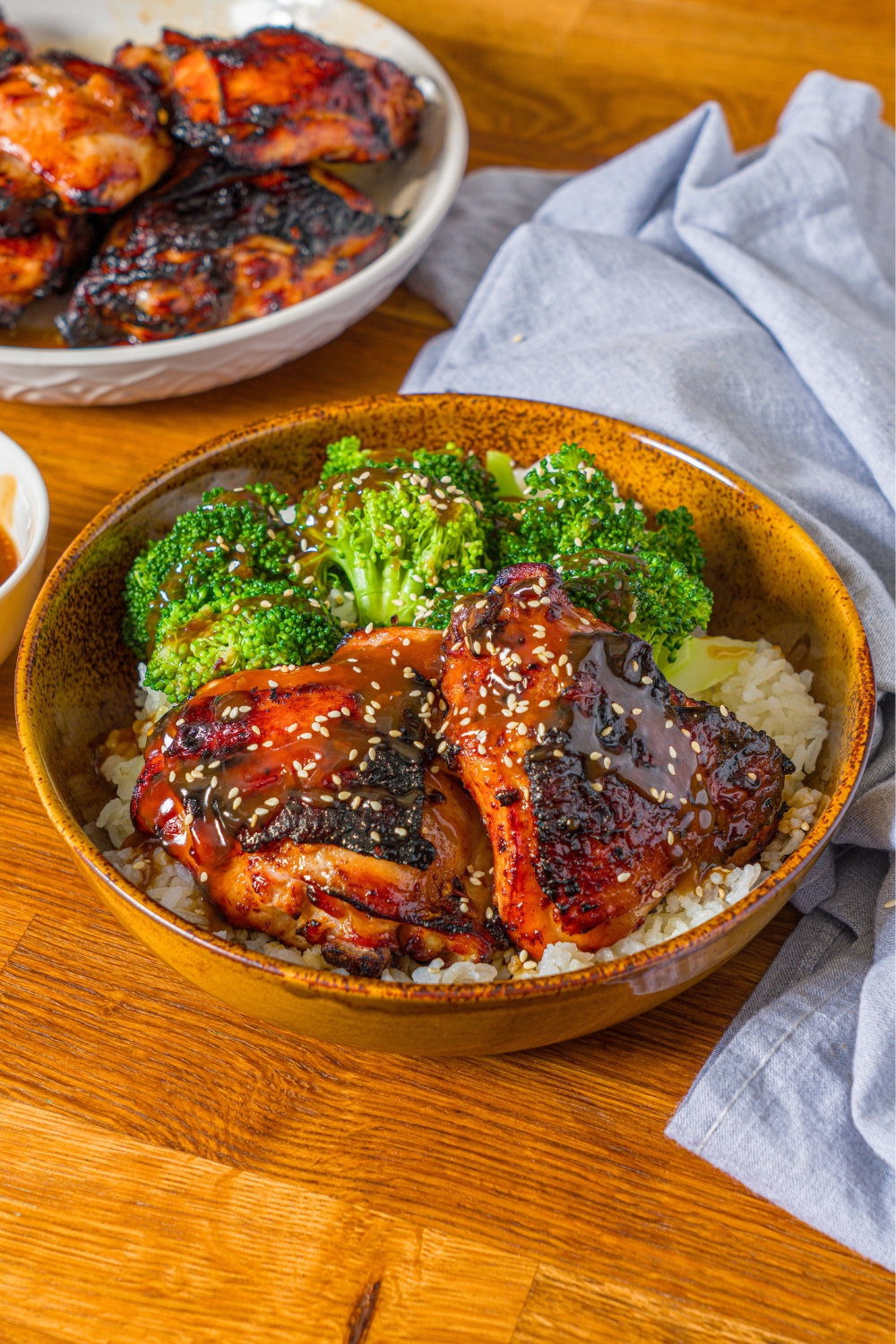 A chicken teriyaki bowl with two chicken teriyaki thighs coated in teriyaki sauce on a bed of basmati rice with broccoli in a wooden bowl.