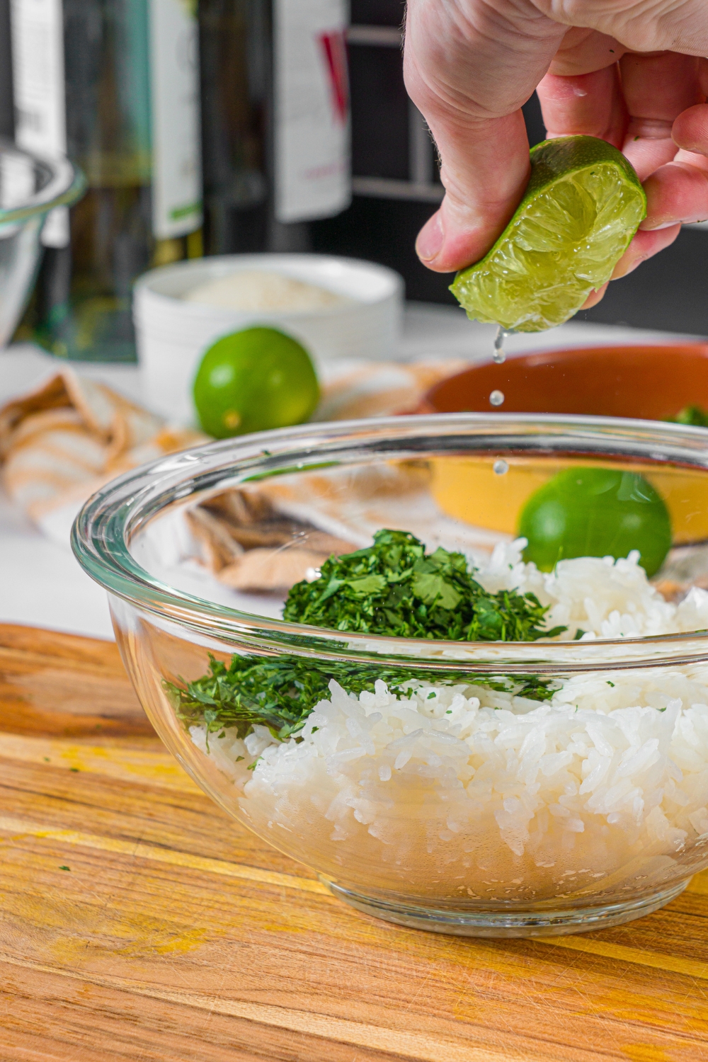 A hand squeezing a lime wedge into a bowl of cilantro and rice.